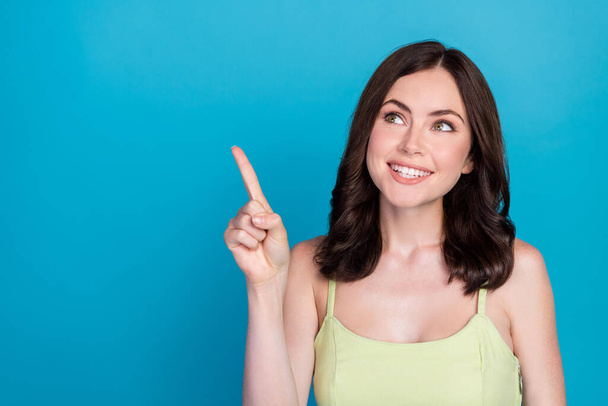 Photo of charming cheerful girl beaming smile look indicate finger empty space isolated on blue color background. - Foto, Imagem