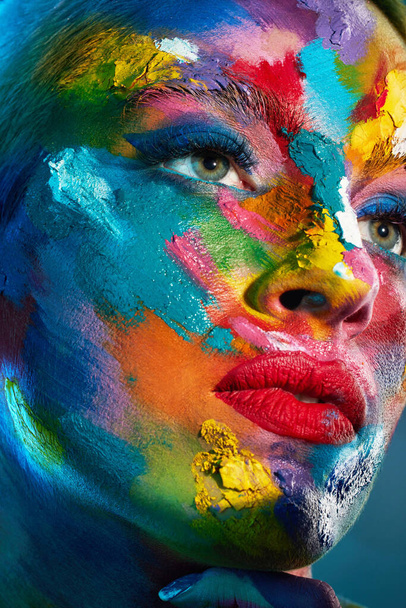 Try to be a rainbow in someones cloud. Studio shot of a young woman posing with multi-coloured paint on her face - Foto, Bild