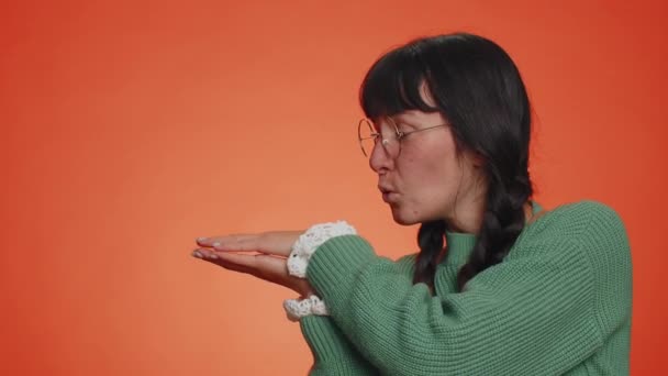 Urocza, tysiącletnia kobieta pokazująca kciuki w górę i wskazująca puste miejsce, obszar reklamowy dla tekstu komercyjnego, przestrzeń do kopiowania promocji towarów. Młoda, dorosła dziewczyna. Studio nakręcone w pomieszczeniu na pomarańczowym tle - Materiał filmowy, wideo