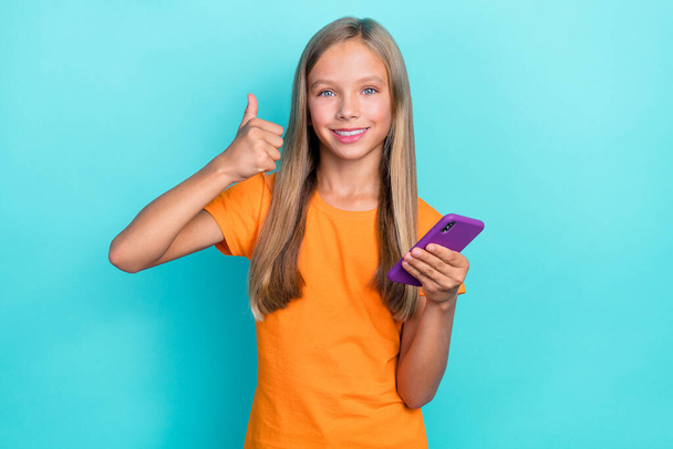 Photo of pretty preteen blogger thumb up satisfied using social media network fast connection gadget isolated on cyan color background. - Zdjęcie, obraz
