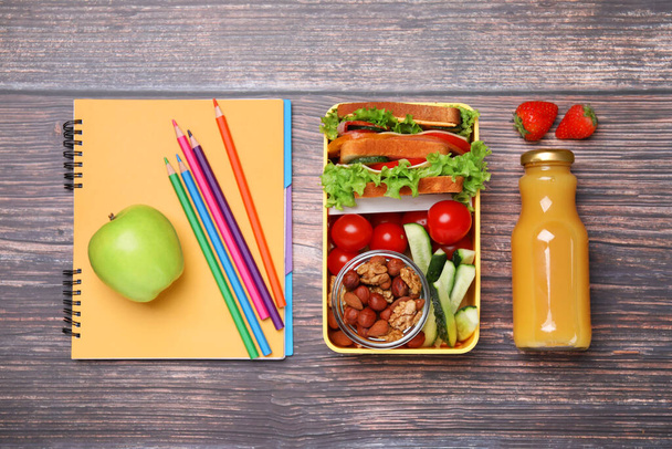 Lunch box with healthy food for schoolchild and different stationery on wooden table, flat lay - Фото, изображение