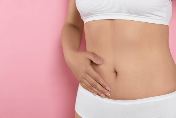 Woman in underwear touching her belly on pink background, closeup. Healthy stomach - Фото, изображение