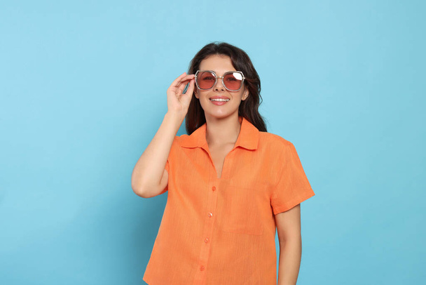 Ευτυχισμένη όμορφη γυναίκα με κομψά γυαλιά ηλίου σε γαλάζιο φόντο - Φωτογραφία, εικόνα