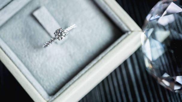 Primer plano de un elegante anillo de diamantes de compromiso en el dedo de la mujer mientras sostiene el teléfono inteligente. amor y concepto de boda. Enfoque suave y selectivo. - Foto, Imagen