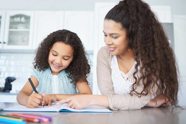 Shes focused and happy, well done mom. a mother helping her daughter with homework at the kitchen table - Фото, изображение