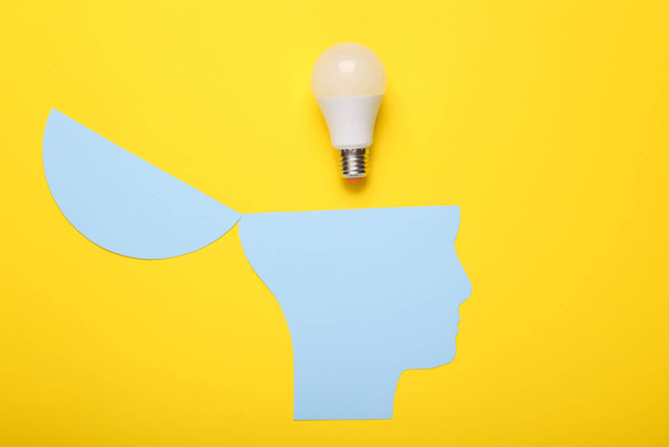 Open your mind, mental health concept, creative thinking. Paper silhouette of human head and light bulb on yellow background - Photo, Image