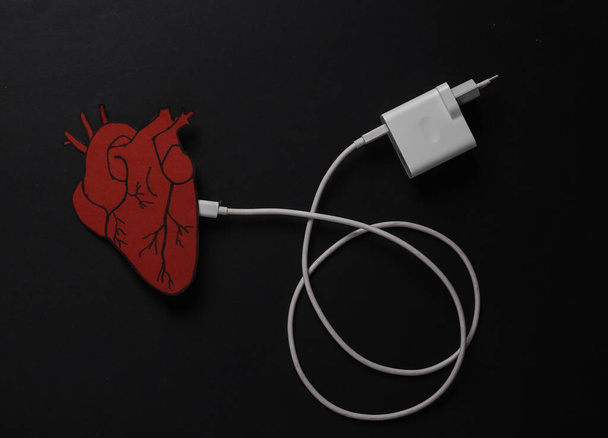 心臓を充電します。黒の背景に充電ケーブル付きの解剖学的心臓。エネルギー料金. - 写真・画像