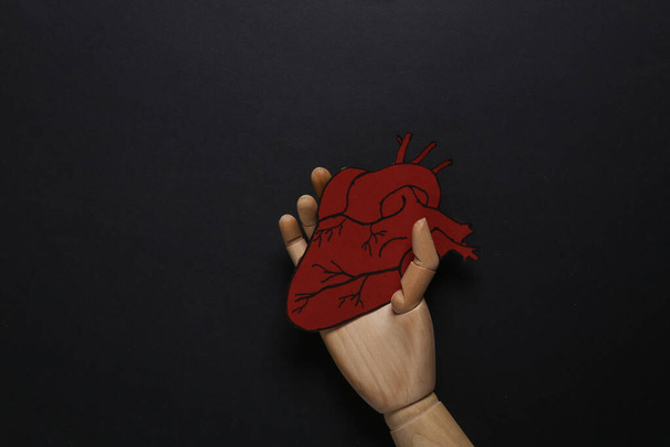 Wooden hand holding Anatomical paper-cut heart on black background. Medicine concept. Healthy and strong heart. Top view - Foto, immagini