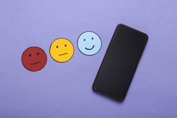Concept d'enquête de satisfaction client. Smartphone, icône de papier visage heureux, neutre et triste sur fond violet. Vue du dessus - Photo, image