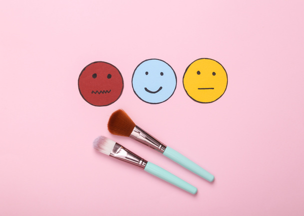 Beauty industry review. Customer satisfaction survey concept. Makeup brushes with happy, neutral and sad face paper icon on pink background. Top view - Foto, Imagem