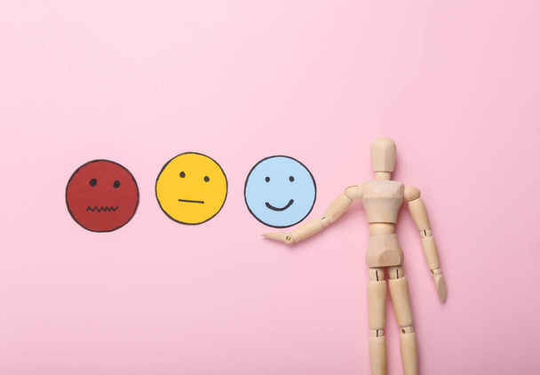 Best service. Customer satisfaction survey concept. Wooden puppet chooses happy face icon, neutral and sad face paper icon on  pink background. Top view - Photo, Image