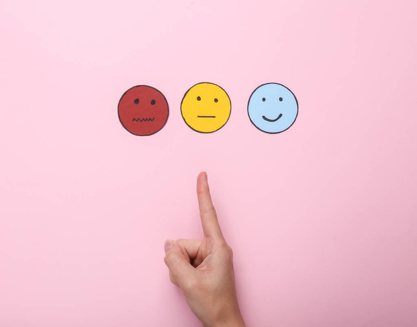 Best service. Customer satisfaction survey concept. Woman hand chooses neutral face icon, happy and sad face paper icon on pink background. Top view - Photo, Image