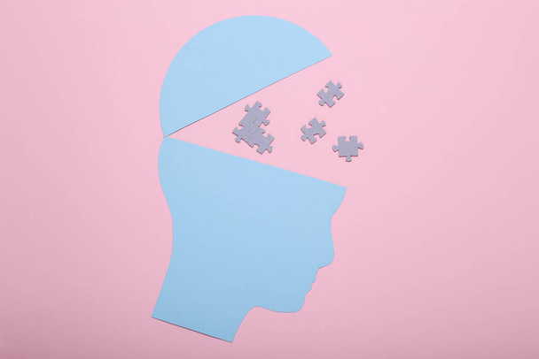 Η έννοια της ανοιχτής συνείδησης, της ψυχικής υγείας, της άνοιας. Σιλουέτα χάρτινης κεφαλής με κομμάτια παζλ σε ροζ φόντο - Φωτογραφία, εικόνα