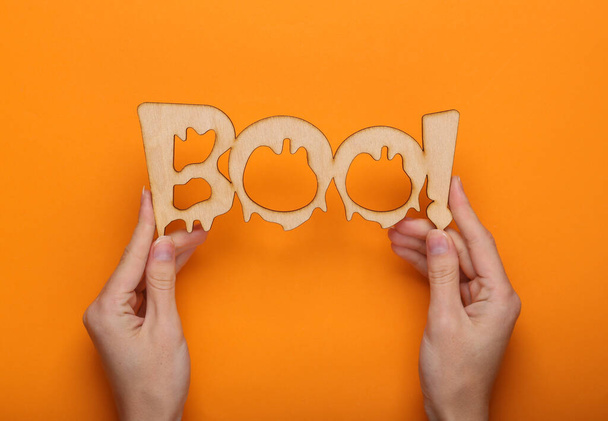 Feliz concepto de Halloween. ¡Manos sosteniendo la palabra boo! sobre fondo naranja. Truco o trato. Vista superior  - Foto, Imagen