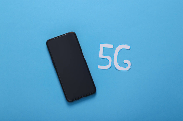 5G-technologie. Smartphone en woord 5g op blauwe achtergrond - Foto, afbeelding