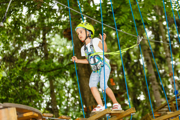 Retrato de niña sonriente en casco y arnés en pista en cielo cuerda parque en verano - Foto, imagen