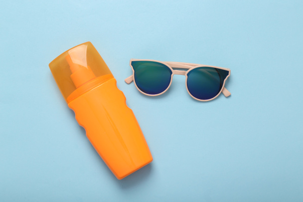 Resort, beach vacation, vacation concept. Sunglasses and a bottle of tanning cream on a blue background. Top view - Foto, Imagen