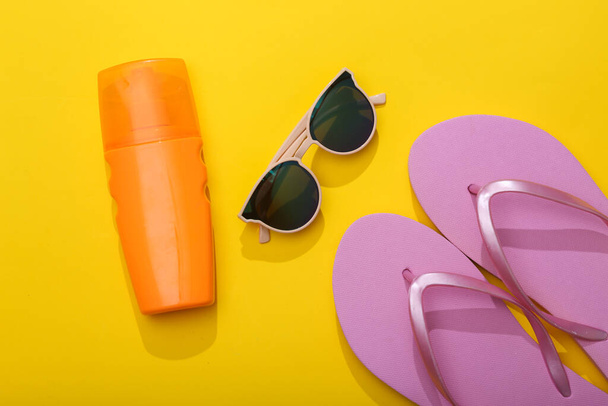 Léto. Resort, plážová dovolená koncept. Sluneční brýle a láhev opalovací krém, žabky na žlutém pozadí. Horní pohled - Fotografie, Obrázek