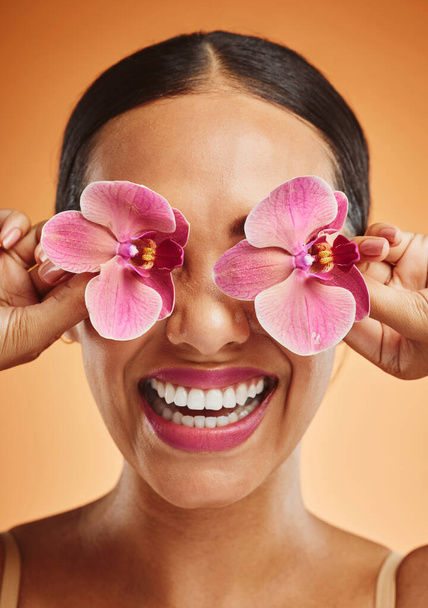 Orchid flower, creative art and beauty woman with makeup, cosmetic and smile on face against an orange background. Happy, floral and comic female model with plant for facial wellness and skincare. - Foto, Bild
