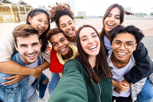 Funny young group of united multiethnic friends taking selfie portrait photo outdoors - Millennial diverse teenager people having fun laughing and celebrating together in street - Community concept - Photo, Image