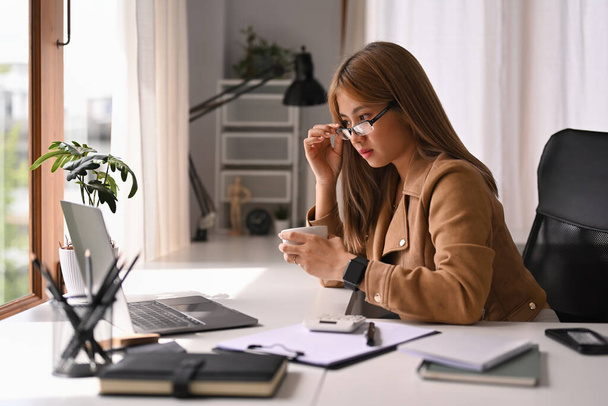 Összpontosított fiatal női kisvállalkozás vállalkozó visel szemüveg olvasás üzleti e-mail laptopon. - Fotó, kép