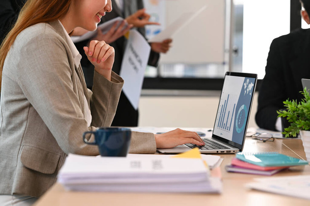 Vista lateral del gerente femenino sentado en la mesa de reuniones y comprobando la información en línea en el ordenador portátil. - Foto, Imagen