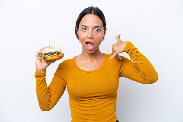 Junge hispanische Frau hält einen Burger isoliert auf weißem Hintergrund und macht Handygesten. Rufen Sie mich zurück - Foto, Bild