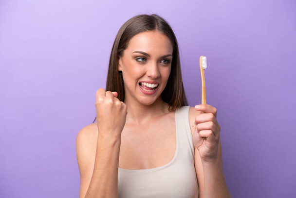 Young caucasian woman brushing teeth isolated on purple background celebrating a victory - Photo, Image