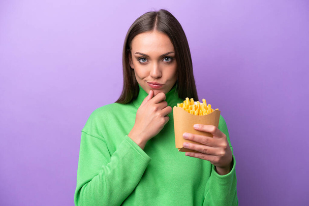 Young caucasian woman holding fried chips on purple background thinking - Φωτογραφία, εικόνα