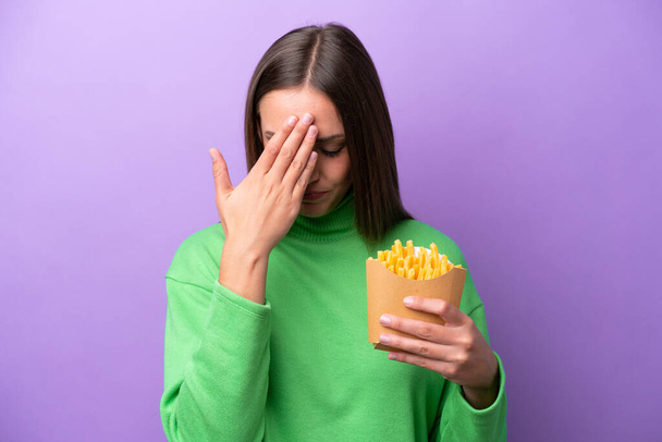 Молода біла жінка тримає смажені чіпси на фіолетовому фоні з втомленим і хворим виразом
 - Фото, зображення