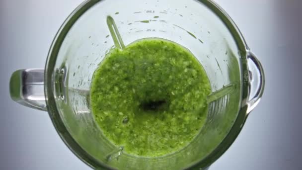 Vegetarian smoothie preparing in electric blender close up top view. Green vitamin blend mixing inside glass bowl in super slow motion. Healthy vegetable cocktail swirling making drops in mixer. - Footage, Video