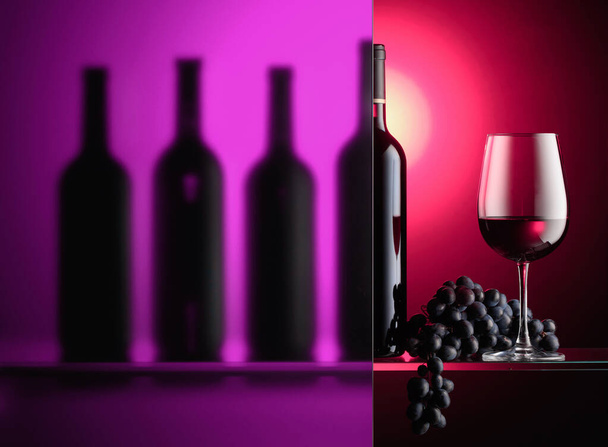 Butelki i kieliszek czerwonego wina z bandą niebieskich winogron. Martwa natura jest częściowo pokryta mrożoną szklanką. Kolor podświetlenia.  - Zdjęcie, obraz