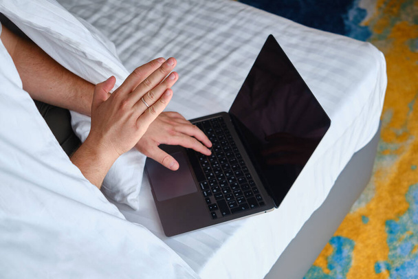 A man businessman sees negotiations through programs, applications on a laptop in bed. Working on a laptop. Business concept. Freelancer at work at home. Online communication - Foto, Imagen
