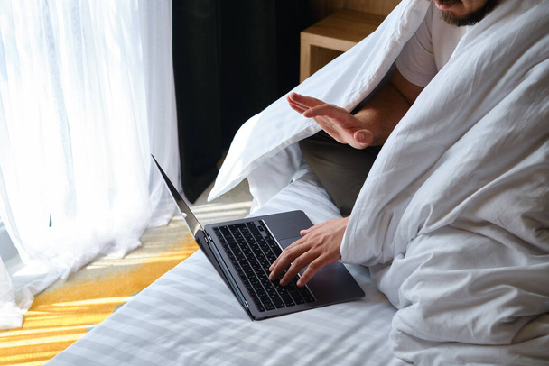 A man businessman sees negotiations through programs, applications on a laptop in bed. Working on a laptop. Business concept. Freelancer at work at home. Online communication - Photo, Image