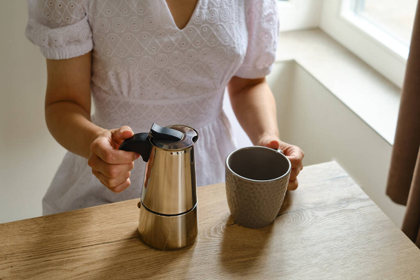 Девушка держит в руках кофейник мока за приготовление горячего свежего кофе. Крупный план металлического кофейника. Оборудование для приготовления кофе. Профессиональное варка кофе - Фото, изображение