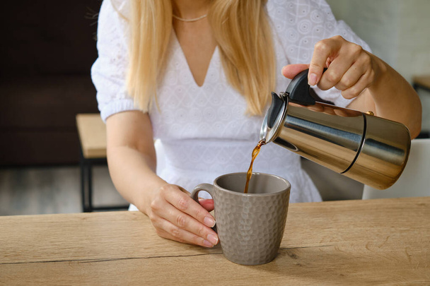 A girl holds a moka pot in her hands for making hot fresh coffee. Close-up of a metal coffee pot. Equipment for making coffee. Professional coffee brewing - Foto, afbeelding