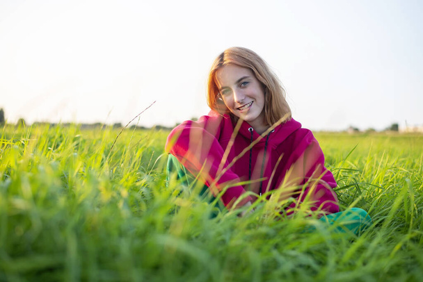 Mutlu genç kız akşam güneşinde çayırda oturuyor. - Fotoğraf, Görsel