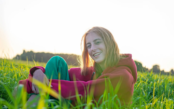 happy young girl sitting on a meadow in evening sun - Photo, Image
