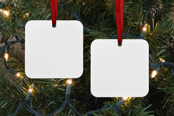 Detailní záběr dvou čtverečních bílých vánočních ozdob visících na rozsvíceném vánočním stromečku. - Fotografie, Obrázek