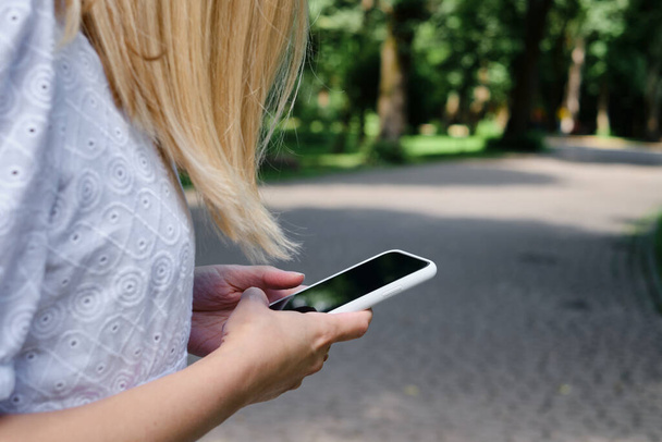 A girl on the street is holding a modern smartphone, sending a text message or using an application on her mobile phone. View city map using smartphone. Smartphone close-up - Foto, Imagen