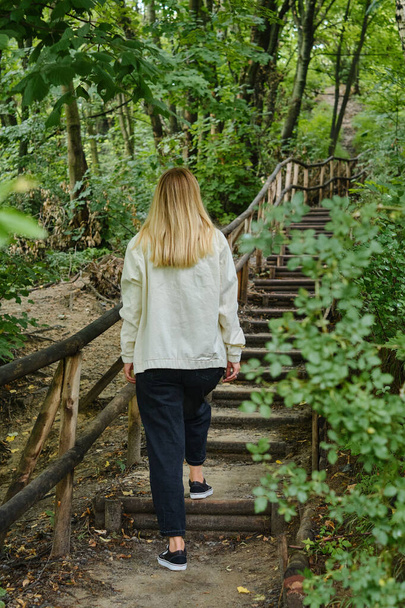 A woman climbs a wooden staircase in a picturesque park. Outdoor activities. Way up the stairs. Walk in nature. Enjoy the weather and fresh air. Weekend in nature - Photo, image