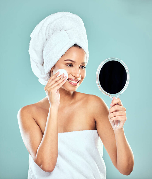 The face of beauty. a young woman applying product to her face with a cotton pad while looking in a mirror against a studio background - Foto, Bild