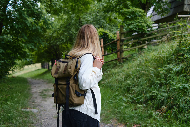 The beautiful girl traveler walks through the village. Beautiful nature landscape in countryside. Hiking journey on tourist trail. Outdoor adventure. Travel and exploration. Healthy lifestyle - Fotoğraf, Görsel