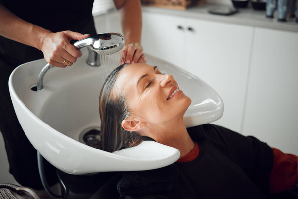 Woman, salon and hair care in wash treatment for beauty, luxury and relax with smile indoors. Happy female enjoying calm relaxation smiling in happiness for clean, service and style by hairdresser. - Φωτογραφία, εικόνα