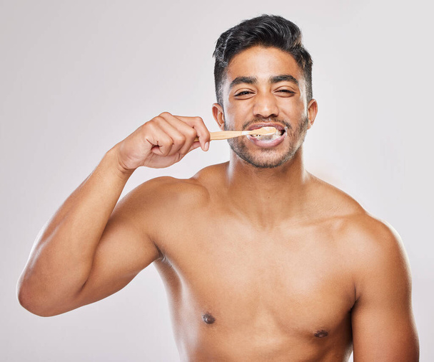 Mijn weg poetsen naar een betere glimlach. een jonge man poetst zijn tanden tegen een grijze achtergrond - Foto, afbeelding
