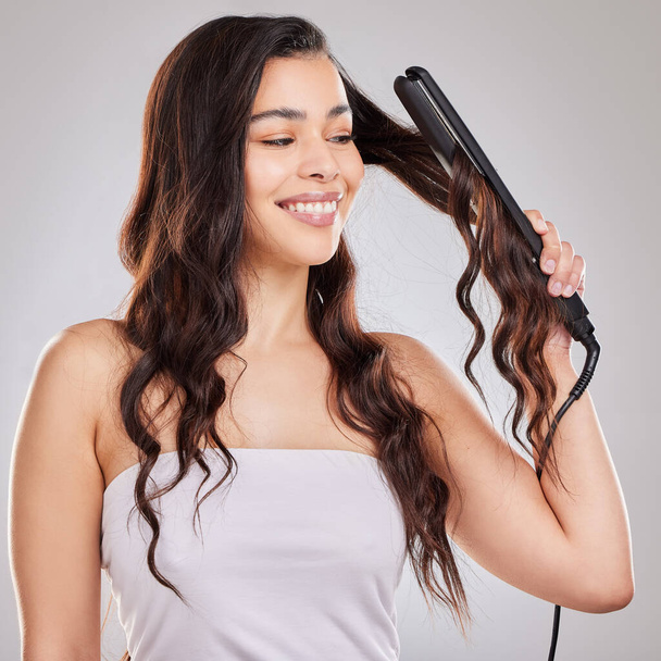 Maybe when you are sad, all you need is a new hairstyle. Studio shot of a beautiful young woman using a straightener on her hair - Фото, изображение