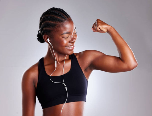 I made no excuses and look at the results. Studio shot of a sporty young woman wearing earphones and flexing her arms against a grey background - Photo, image