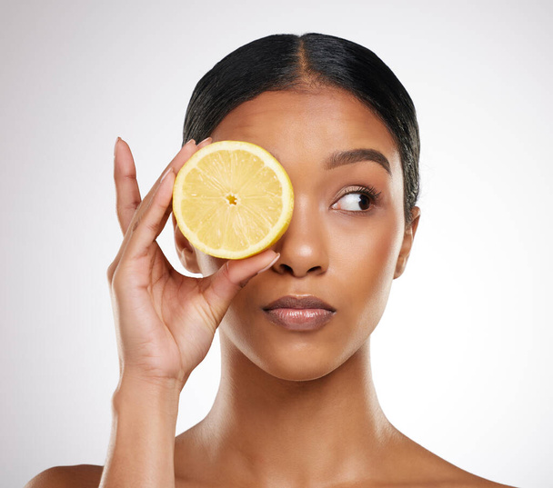 Vitamin See. Studio shot of an attractive young woman posing with half a lemon against a grey background - Fotó, kép