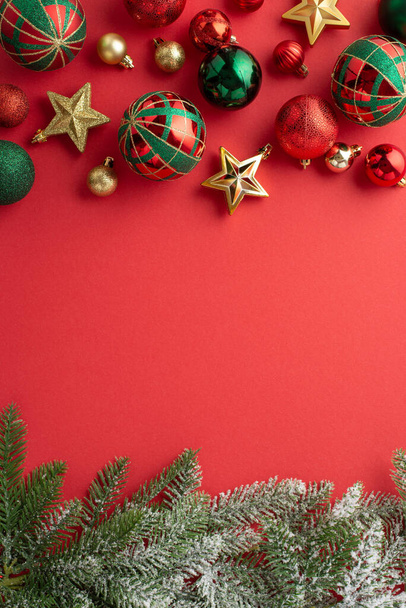Koncepcja Święta Bożego Narodzenia. Widok z góry pionowe zdjęcie gałęzi sosny w śniegu gwiazdy ozdoby złoty zielony i czerwony bombki na izolowanym czerwonym tle z copyspace - Zdjęcie, obraz