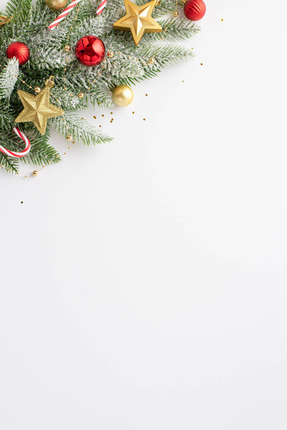 Koncepcja Święta Bożego Narodzenia. Widok z góry pionowe zdjęcie gałązki sosny w mrozie ozdobione czerwonymi bombkami złote ozdoby cukierki laski i konfetti na odizolowanym białym tle z copyspace - Zdjęcie, obraz